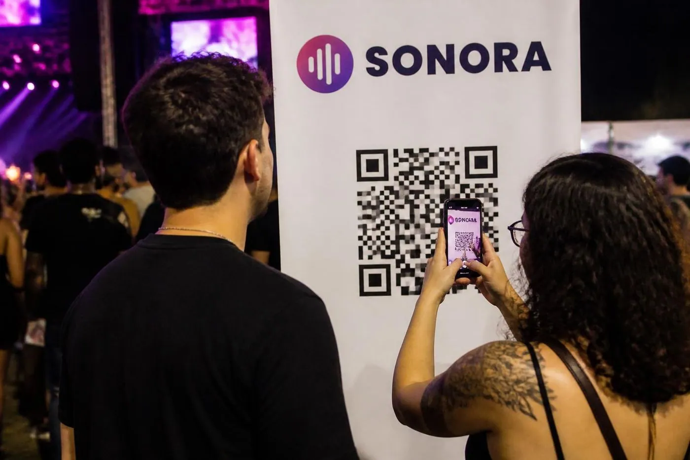 Amigos lendo o QR code de um banner num festival de música