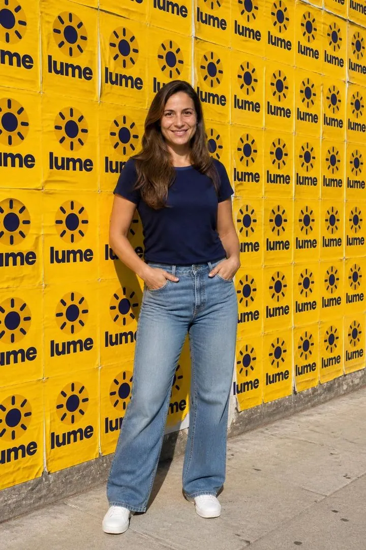 Exemplo com IA: convidada diante de um muro coberto de lambes da marca fictícia lume