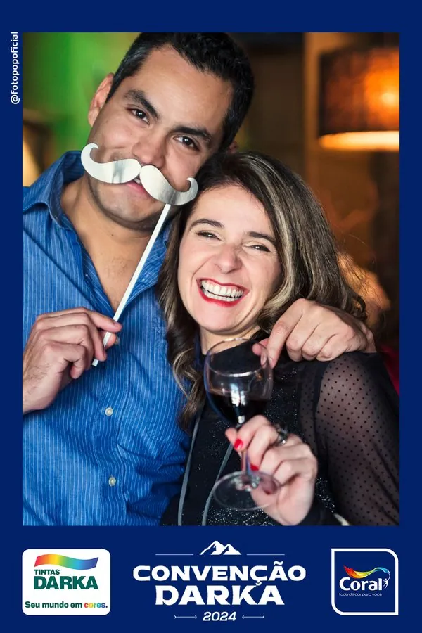 Foto impressa com o layout da Convenção Darka 2024: casal com bigode de festa e os logotipos da Tintas Darka e da Coral