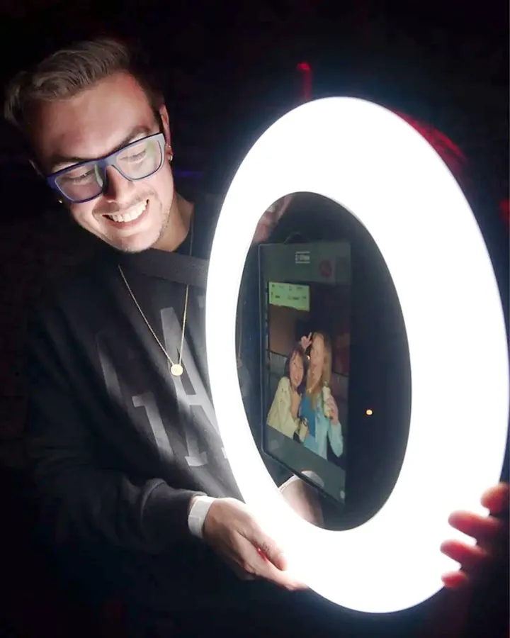 Convidado sorrindo atrás do SelfiePop, o tablet com ring light, que mostra a foto